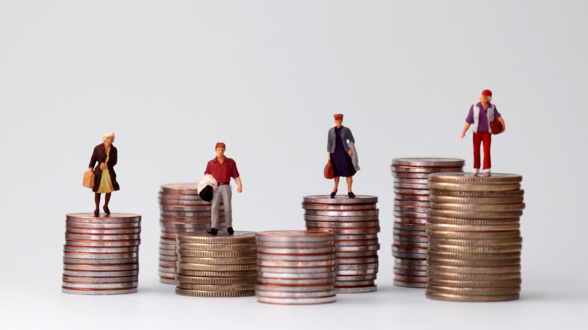 Miniature people standing on piles of different heights of coins.