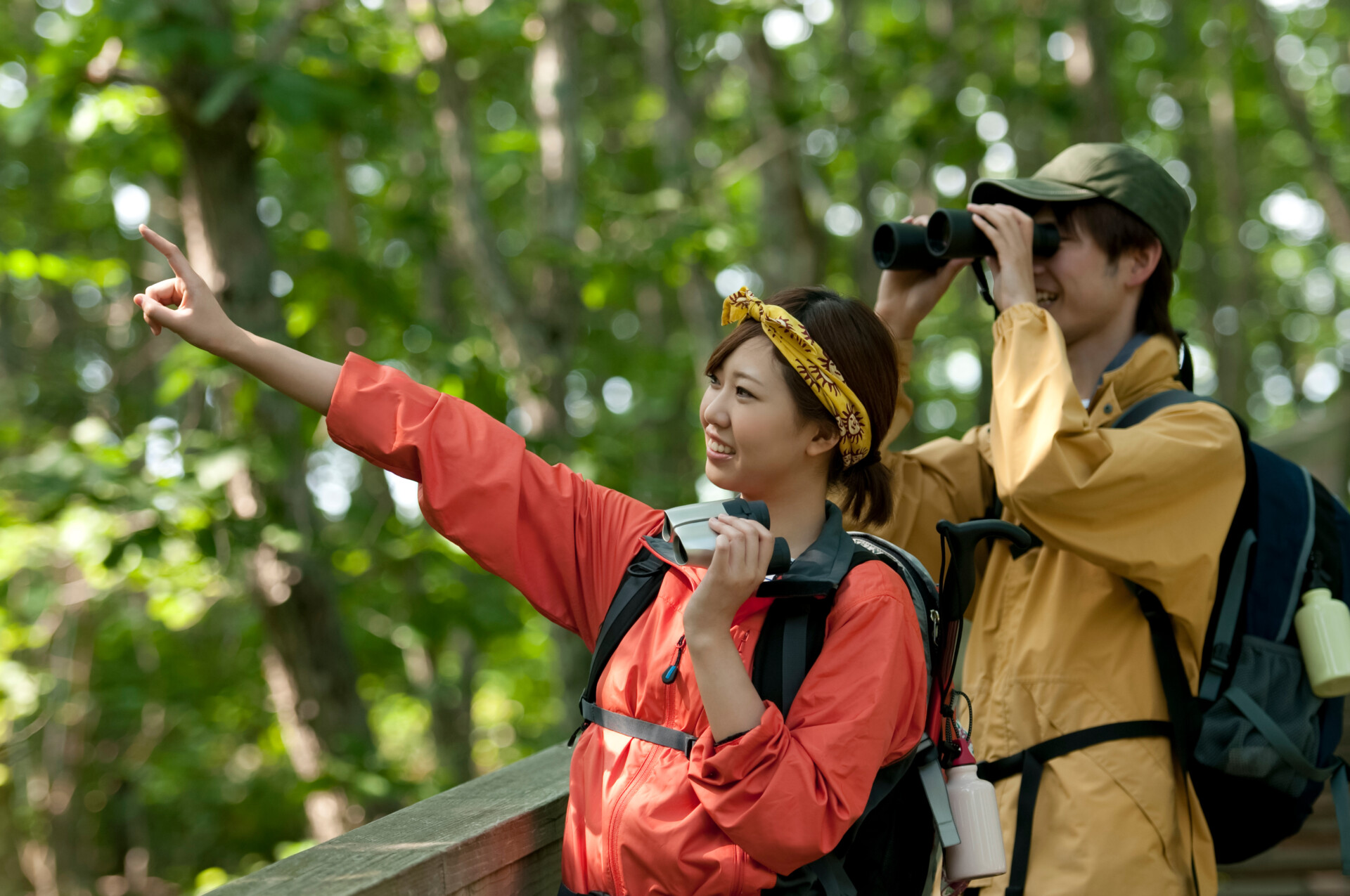 a couple bird watching. one person points off into the distance while the other looks through binoculars.