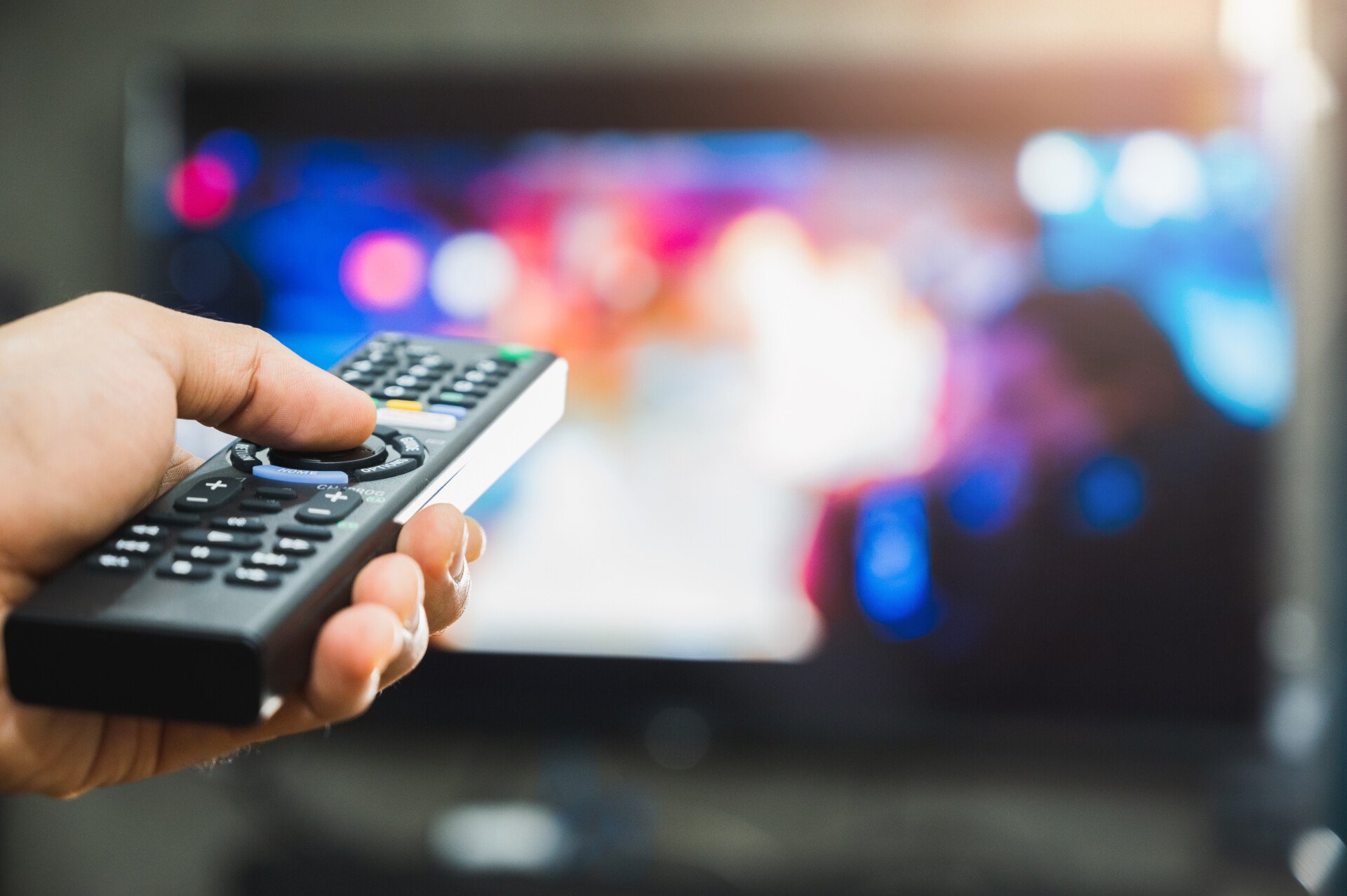 Young man holding television remote control. Hands pointing to tv screen set and turning it on or off select channel watching tv on his sofa at home in the living room relax.