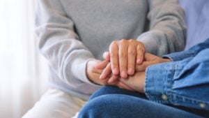 A close up of two people clasping hands in an empathetic way.